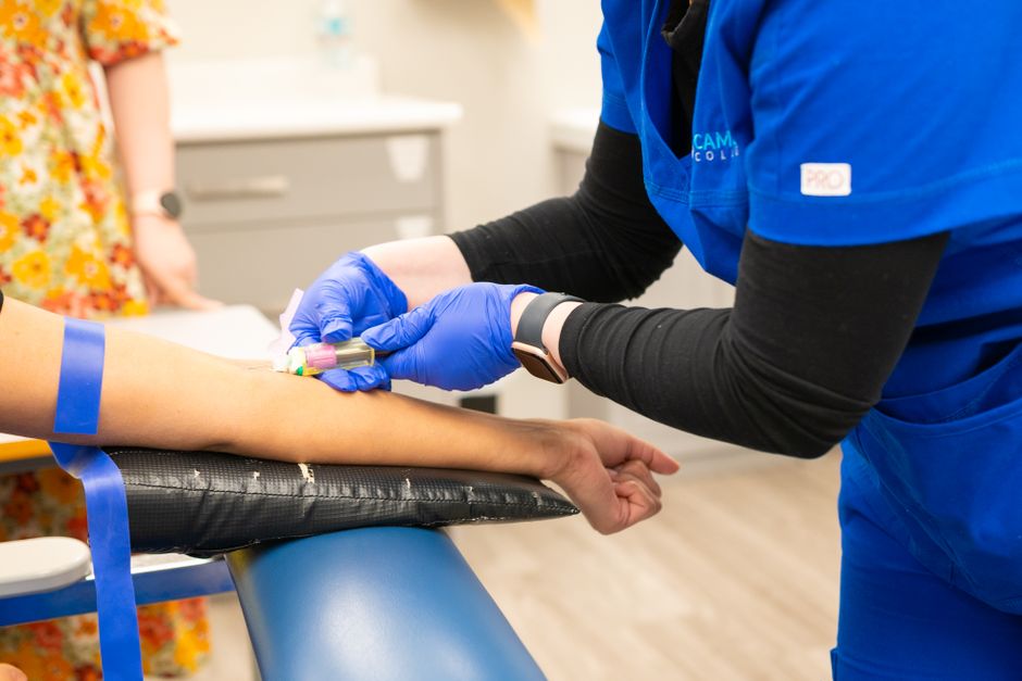 Nurse performing blood draw with blue gloves in medical clinic setting.