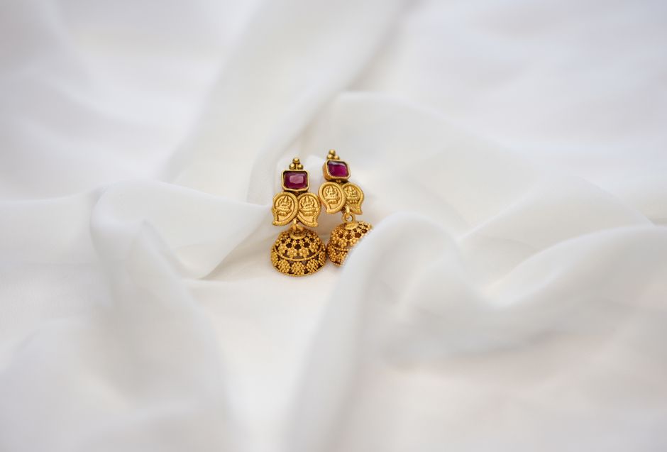 Elegant gold jhumka earrings with ruby accents displayed on white fabric, perfect for occasions.