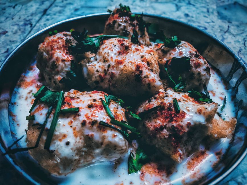 Close-up of traditional Indian dahi vada garnished with yogurt, herbs, and spices.