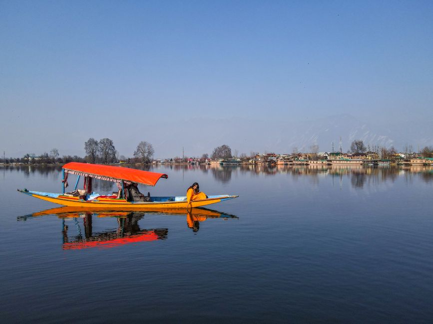 Colorful shikara boat with woman on Dal Lake, reflecting scenic beauty of Kashmir.